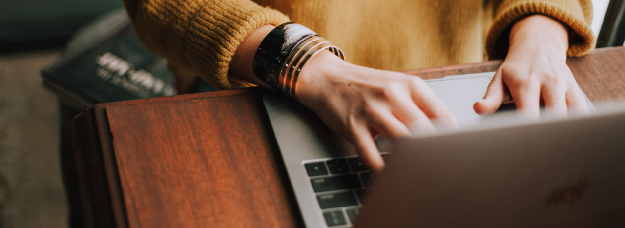 Woman typing on laptop wearing yellow sweater and bracelets